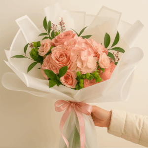 Ramo Dulce Encanto Fioretta con rosas y hortensias en tonos durazno pastel, envuelto en papel blanco y lazo rosa. Arreglo floral elegante y romántico Fioretta.