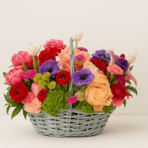 Canasto floral colorido con tulipanes, anémonas, ranúnculos, claveles y peonías en tonos coral, violeta y rojo, presentado en canasto celeste — Fioretta Chile