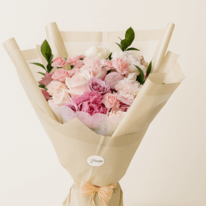 Ramo Dulce Époque Fioretta con flores pastel en tonos rosado, crema y lavanda. Arreglo floral elegante Fioretta envuelto en papel beige con lazo de organza.