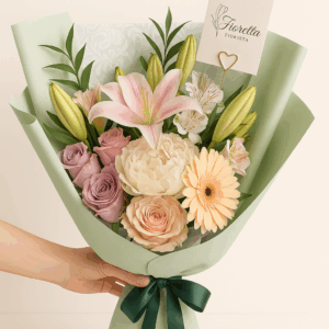 Ramo Serenidad Fioretta con rosas, lirios y flores pastel en tonos crema, durazno y lila, envuelto en papel verde salvia con lazo esmeralda. Arreglo floral elegante y delicado Fioretta.