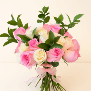 Ramo Susurro de Rosas Fioretta con rosas rosadas y marfil, follaje verde y lazo rosa de organza. Arreglo floral romántico y elegante Fioretta.